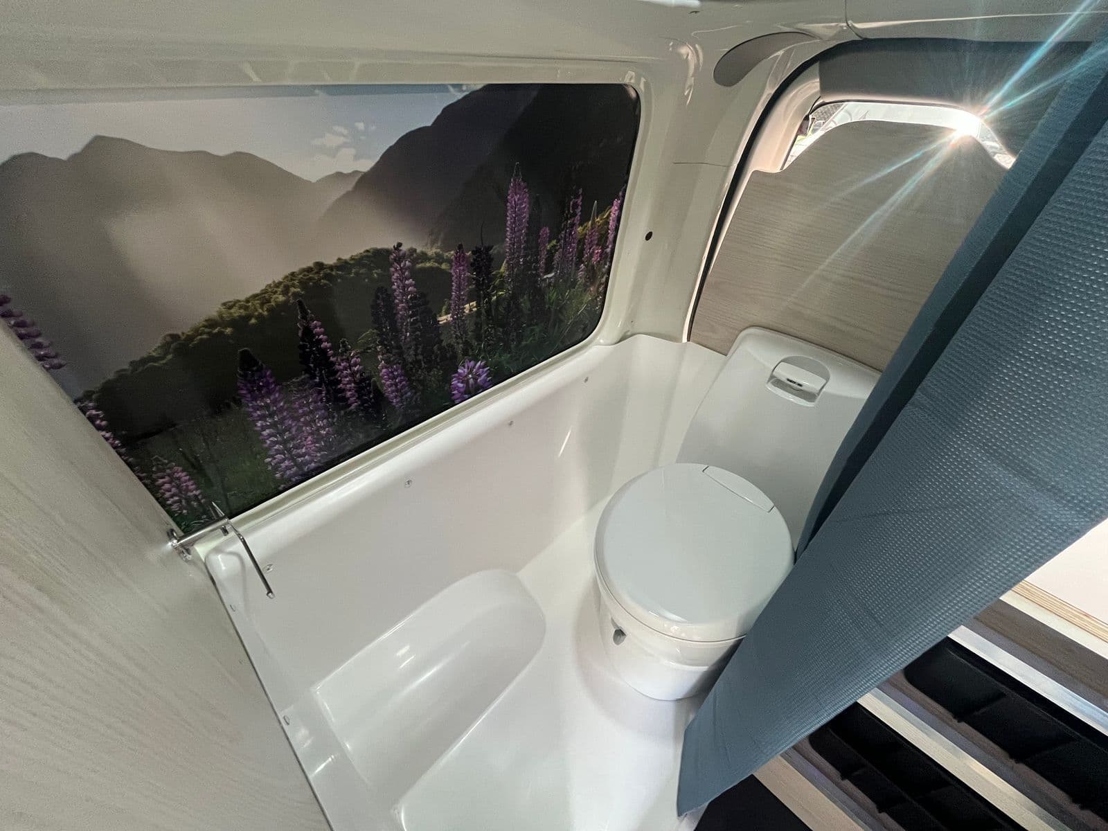 Moulded white toilet cubicle with a fixed flush toilet, behind a fabric curtain