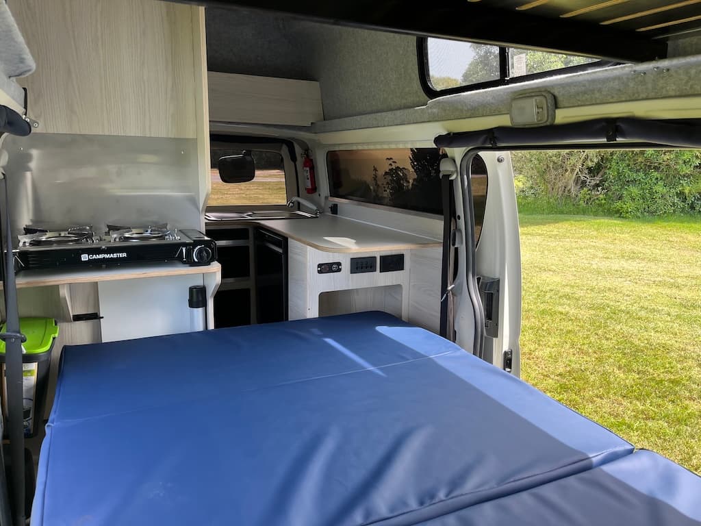 Lower double bed made up across the campervan with the side door open to grass