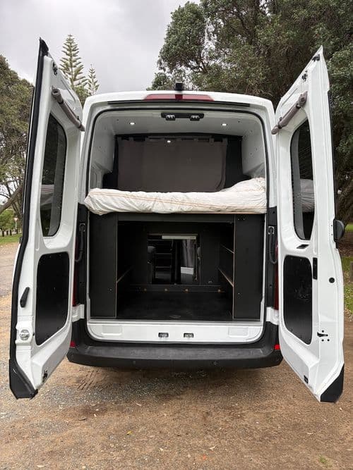 Rear doors of the van open, showing a made-up double bed above an empty storage garage