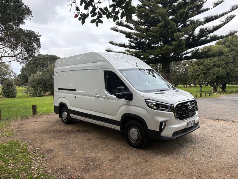 White high-roof LDV Deliver 9 van parked on gravel under large trees