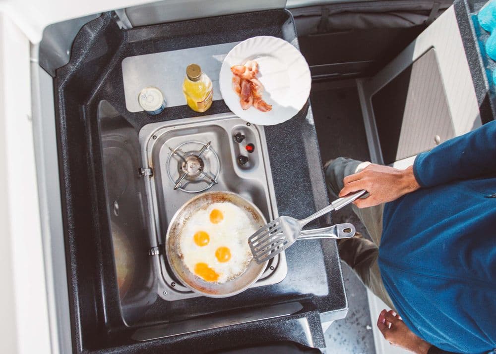 Overhead view of the campervan kitchen with a gas burner, sink and a pan of eggs cooking