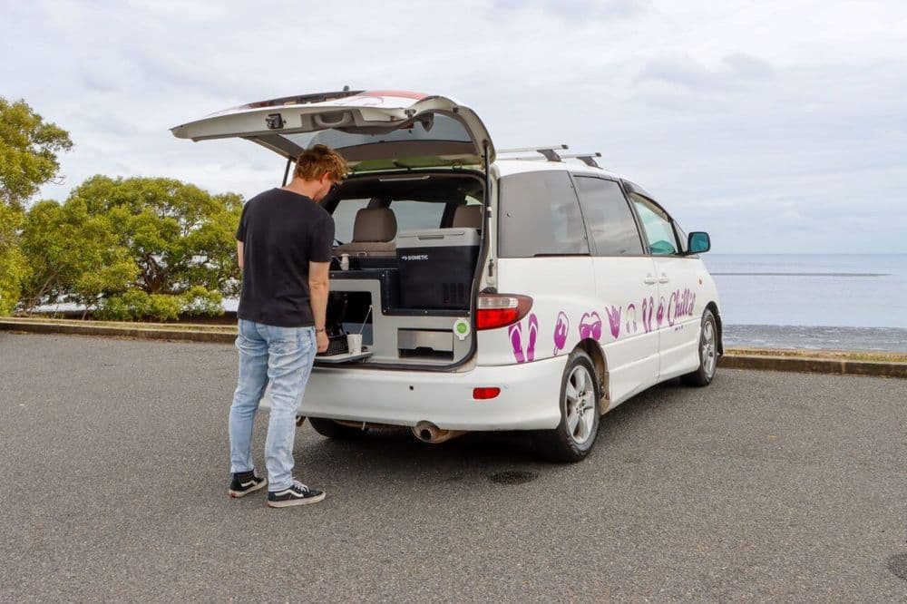 Man standing at the open rear hatch of the campervan using the slide-out kitchen unit
