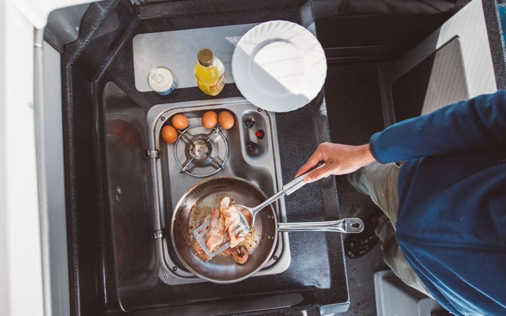 Overhead view of the campervan kitchen with a gas burner, a stainless sink and a frying pan of eggs